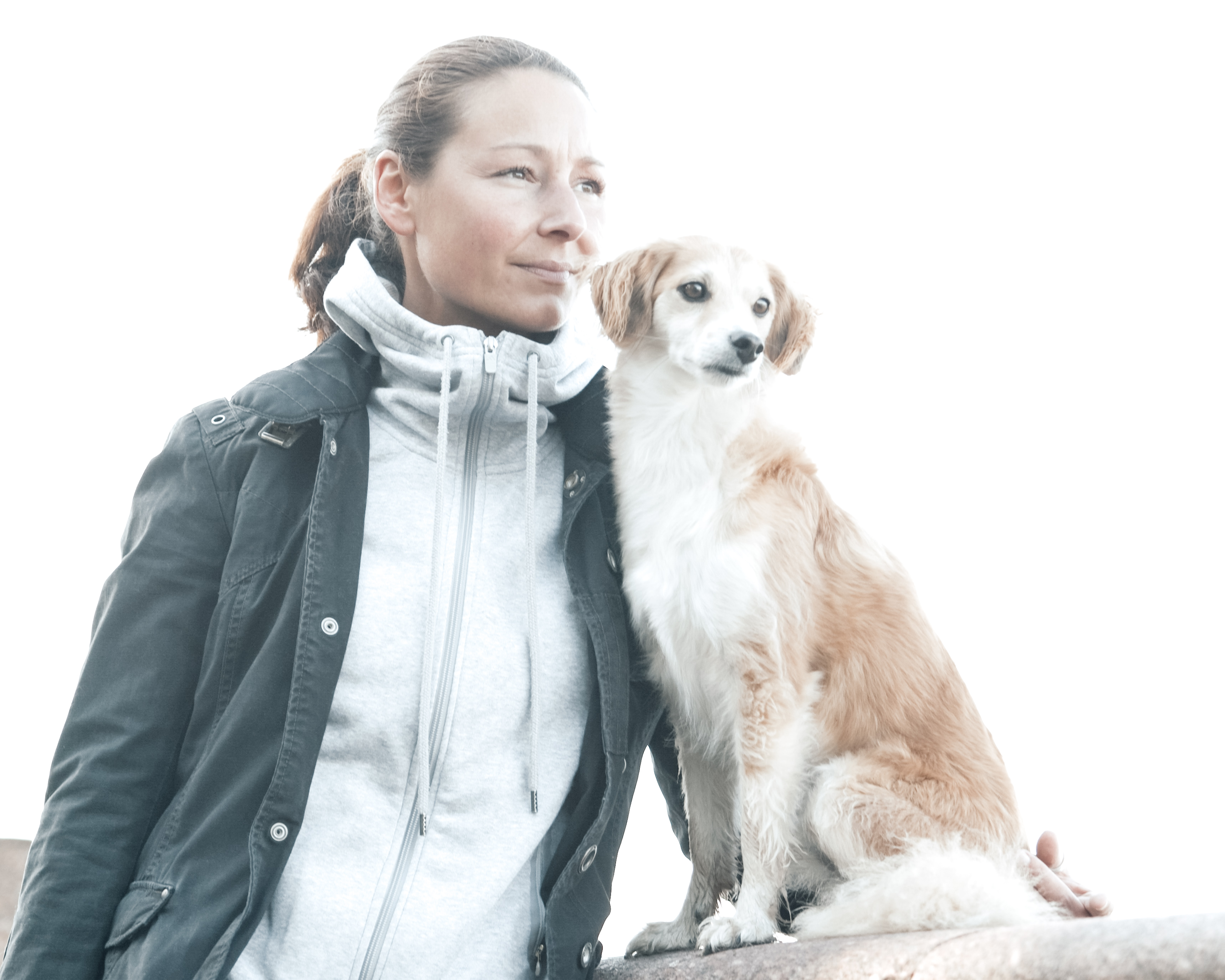 Eine Frau steht ruhig neben einem Hund, beide blicken in die Ferne.